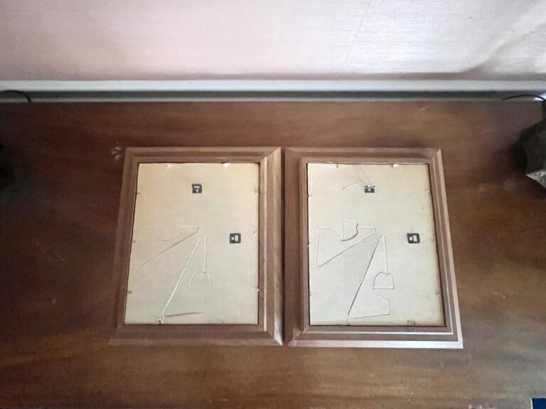Two empty, back-side-up picture frames with hanging wires on a wooden surface.