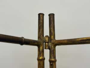 Close-up of two intersecting, weathered rods from a Maison Bagues Gilt Bamboo Metal Folding Screen set against a plain light background.
