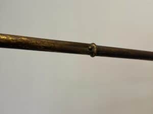 A close-up of the Maison Bagues Gilt Bamboo Metal Folding Screen shows its aged, weathered metal rod with a small raised ring in the middle, set against a plain background.