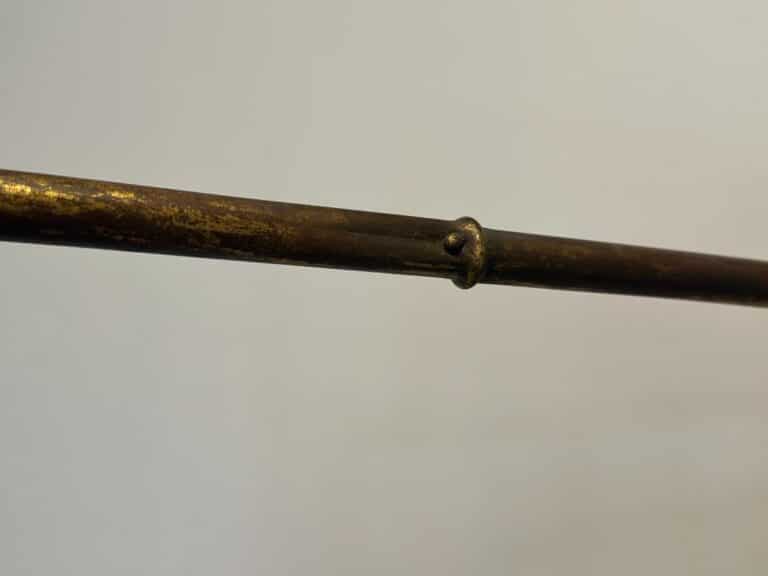 A close-up of the Maison Bagues Gilt Bamboo Metal Folding Screen shows its aged, weathered metal rod with a small raised ring in the middle, set against a plain background.