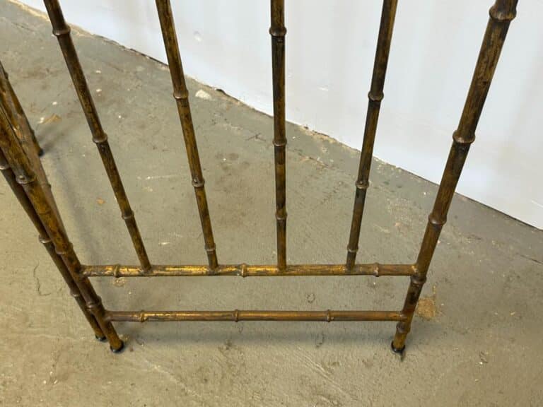 The Maison Bagues Gilt Bamboo Metal Folding Screen features brass-colored metal rods designed to resemble bamboo, showcased here as part of its decorative frame on a concrete floor.