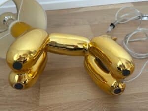 A gold balloon dog-shaped lamp lying on a wooden floor with its cord visible.
