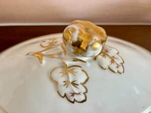 Close-up of a porcelain lid with gold leaf and vine decorations, featuring a gold-accented handle.