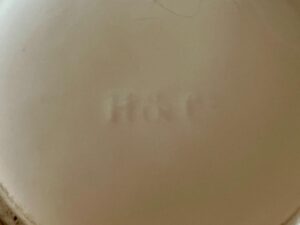 Faded impression with letters "M & C" on a beige surface.