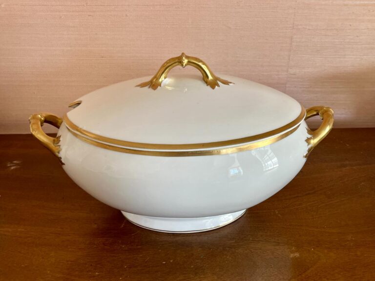 White porcelain tureen with gold trim and handles on a wooden table.