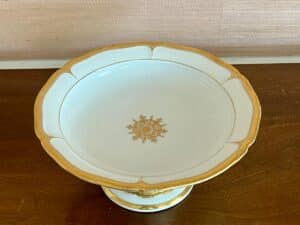 An ornate porcelain pedestal bowl with gold accents and a decorative design at the center.