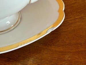 A white and gold plate with a chip on the edge, resting on a wooden surface.