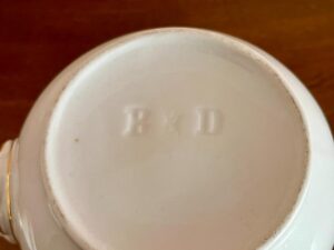 Underside of a white ceramic item marked with embossed letters "B & D," on a wooden surface.