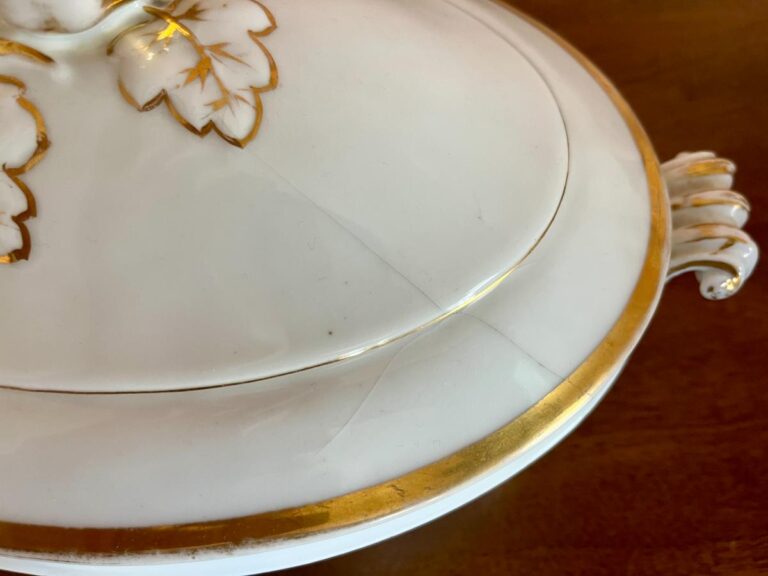 White porcelain dish with gold rim and leaf accents on lid, placed on a wooden surface.