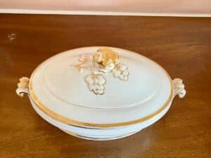 White ceramic serving dish with a lid, gold trim, and floral design, on a wooden surface.