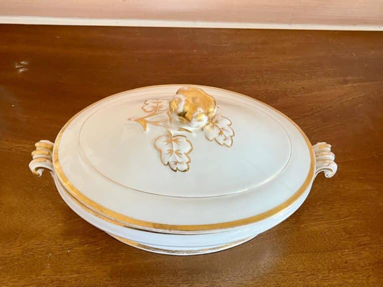 White ceramic serving dish with a lid, gold trim, and floral design, on a wooden surface.