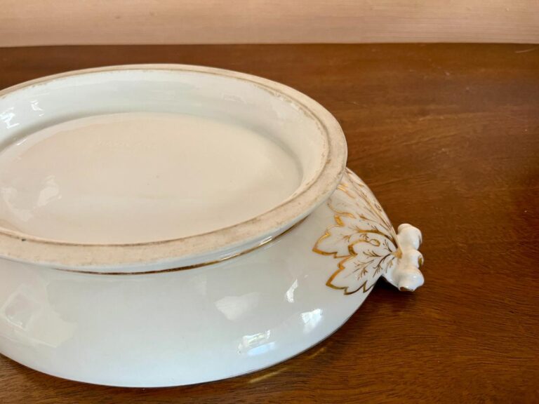 White ceramic dish with lid on a wooden table, featuring a floral design with gold accents.