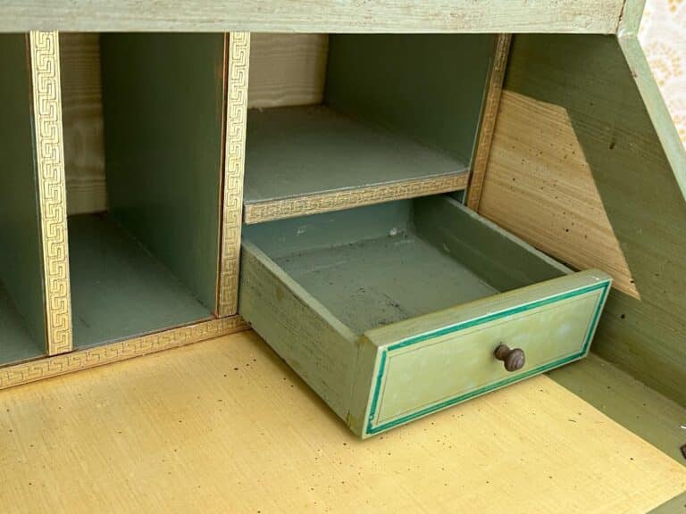 Green vintage desk with an open small drawer, featuring gold accents, on a light wood surface.