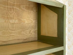 Wooden shelf with olive green trim against a patterned wallpaper background.
