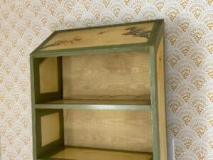 Wooden shelf with green trim against patterned wallpaper, featuring a nature design on the top panel.