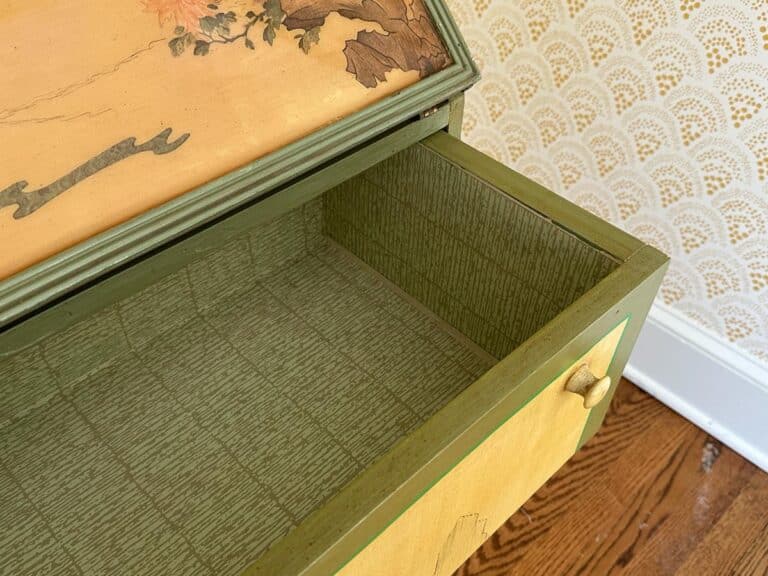 Open green drawer with floral design, showing empty interior and patterned wallpaper background.