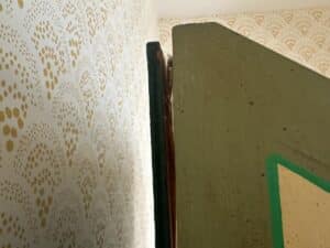 Close-up of a slightly open green door against a wall with gold patterned wallpaper.