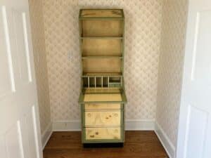 Wooden hutch with drawers and shelves, featuring green and natural finish, against vintage wallpaper.