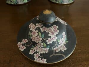 A pair of Black Floral Famille Noir Style Urns with a pink cherry blossom design on a dark background, resting on a wooden surface.