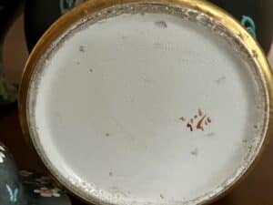 Bottom of a black floral Famille Noir style urn with handwritten markings amidst dark floral decor.