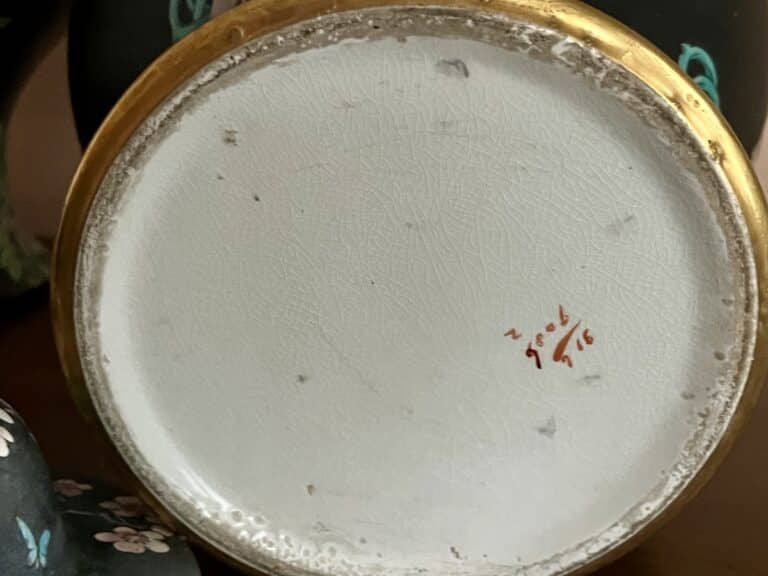 Bottom of a black floral Famille Noir style urn with handwritten markings amidst dark floral decor.