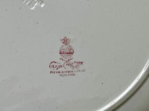 Red pottery mark with crown and text on a white ceramic surface.
