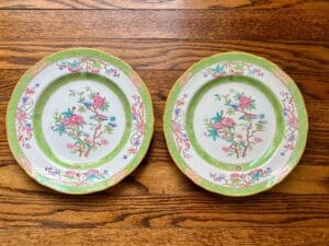 Two ornate plates with floral and bird designs, featuring green rims, on a wooden surface.