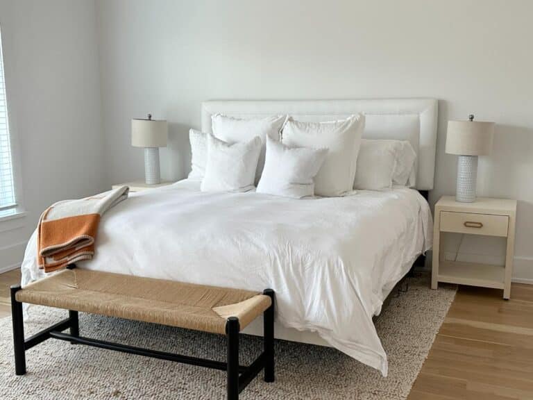 Modern bedroom with white bedding, two bedside tables with lamps, and a bench at the foot of the bed.