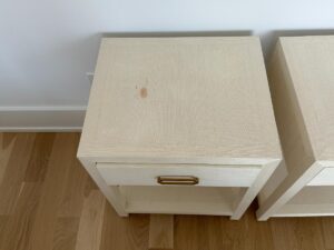 Light-colored wooden nightstand with a drawer, gold handle, and visible stain mark on the top surface.