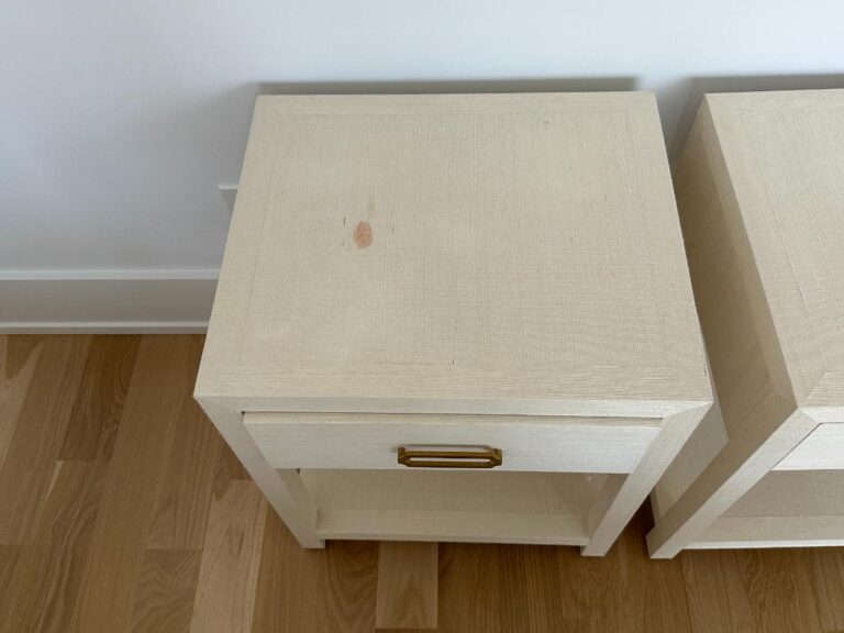 Light-colored wooden nightstand with a drawer, gold handle, and visible stain mark on the top surface.