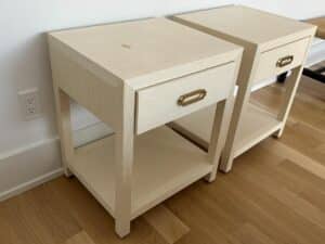 Two light-colored wooden nightstands with drawers and brass handles, placed side by side on a wood floor.