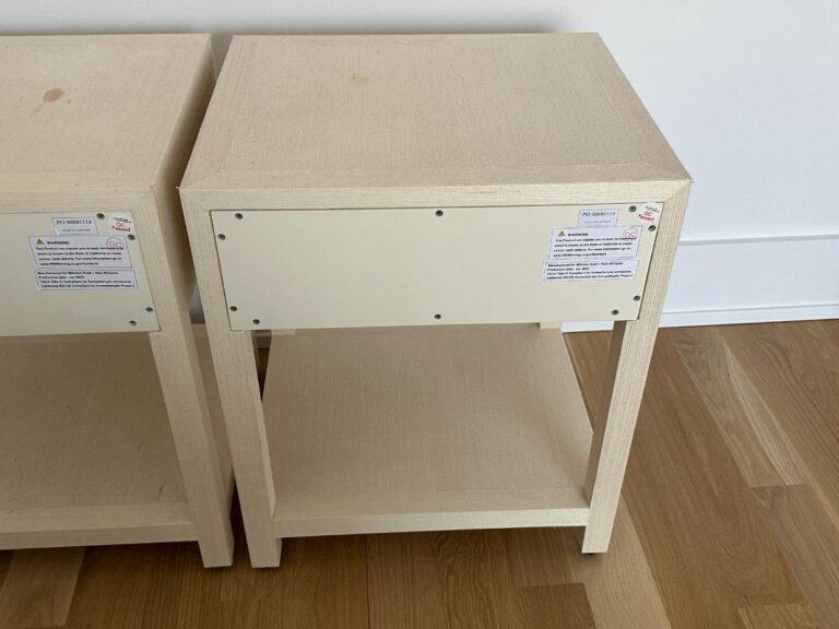 A light wood nightstand with an open shelf and a white panel on the back, placed on a wooden floor.