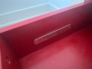 Close-up of a red drawer with a metal label reading "Mitchell Gold + Bob Williams.