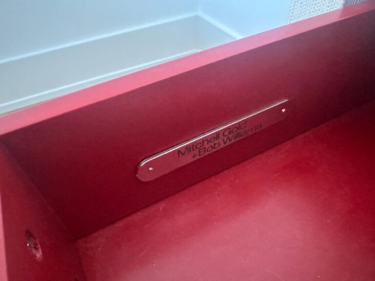 Close-up of a red drawer with a metal label reading "Mitchell Gold + Bob Williams.