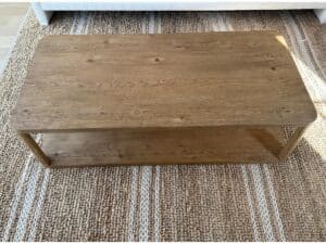 Rectangular wooden coffee table with a lower shelf, placed on a woven rug.