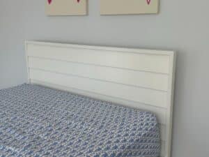 White headboard and blue-patterned bedspread with two partial wall art pieces above.