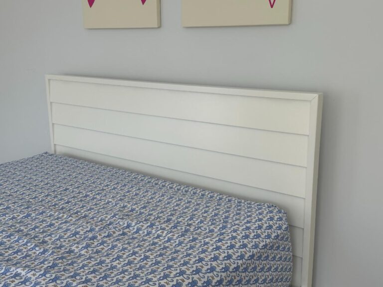 White headboard and blue-patterned bedspread with two partial wall art pieces above.