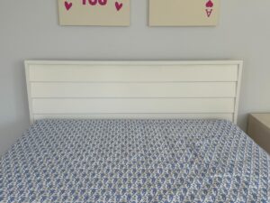 A bed with a white headboard and a blue patterned bedsheet, under wall art with hearts and the words "YOU" and "A".