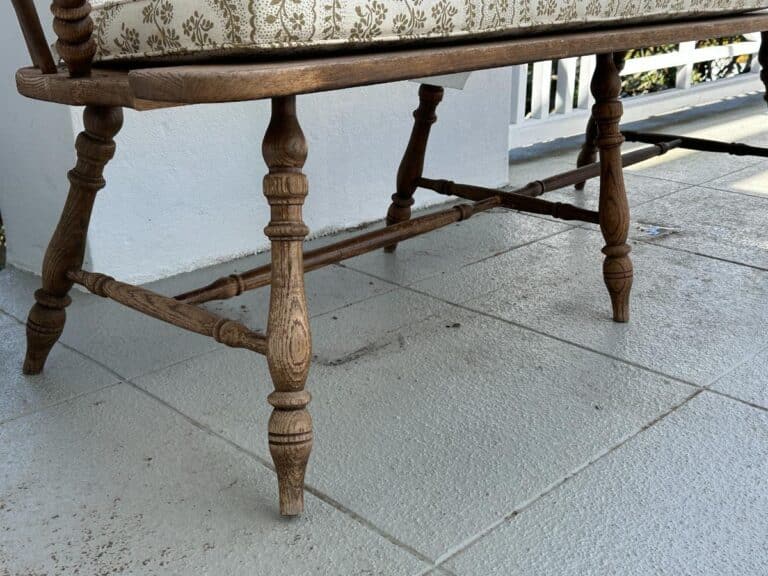 Wooden bench with ornate legs and a patterned cushion on a tiled porch.