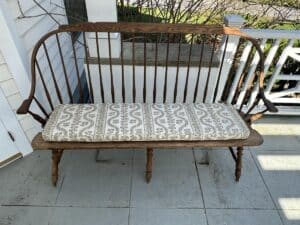 Wooden bench with decorative backrest and patterned cushion, placed on a porch next to a white railing.