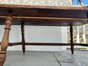 Low-angle view of a wooden table with ornate turned legs on a tiled patio with decorative wall in the background.