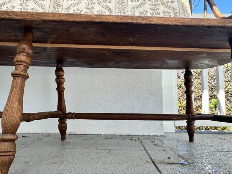 Low-angle view of a wooden table with ornate turned legs on a tiled patio with decorative wall in the background.