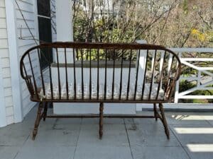 Wooden bench with cushion on a porch, overlooking a garden area.