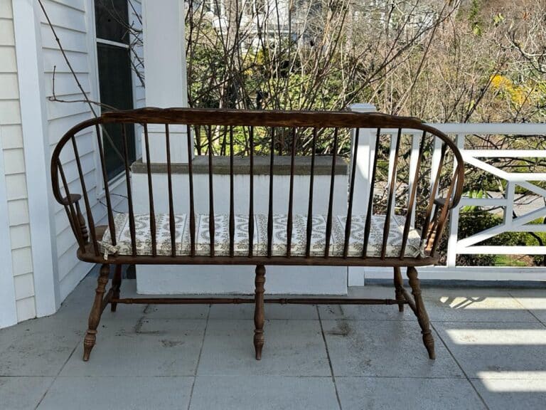 Wooden bench with cushion on a porch, overlooking a garden area.