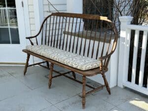Wooden bench with a patterned cushion on a porch, next to a white railing and door.