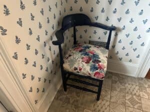 A blue painted corner chair with a Cowtan & Tout seat is set against patterned wallpaper.