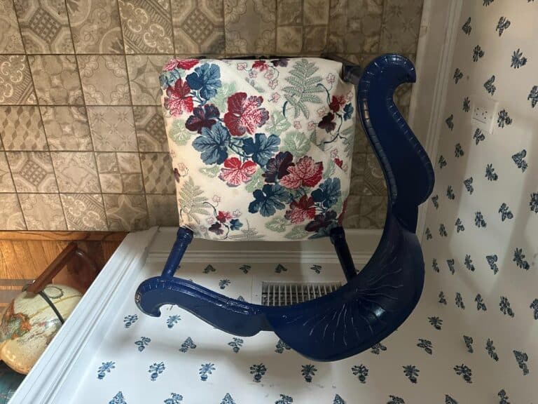 Blue Painted Corner Chair with Cowtan & Tout Seat, inverted with floral upholstery on a patterned floor and wall background.
