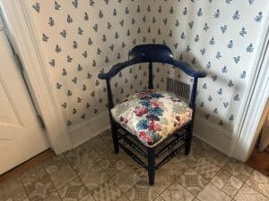 A blue painted corner chair with a Cowtan & Tout seat sits in a corner against butterfly-patterned wallpaper.