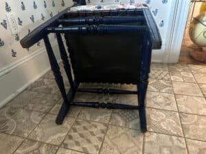 A Blue Painted Corner Chair with Cowtan & Tout Seat lies flipped upside down on a patterned tile floor.