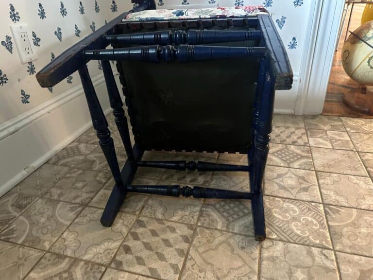 A Blue Painted Corner Chair with Cowtan & Tout Seat lies flipped upside down on a patterned tile floor.